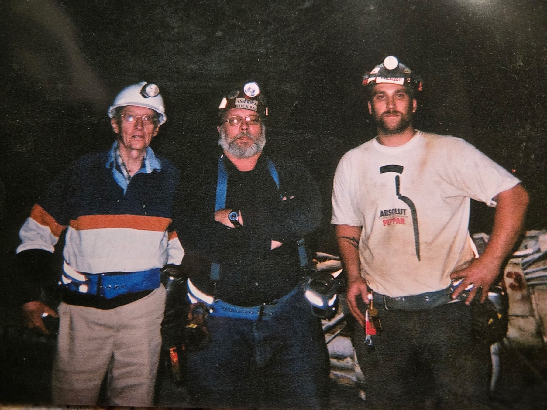 Three miners wearing hard hats and headlamps together underground.